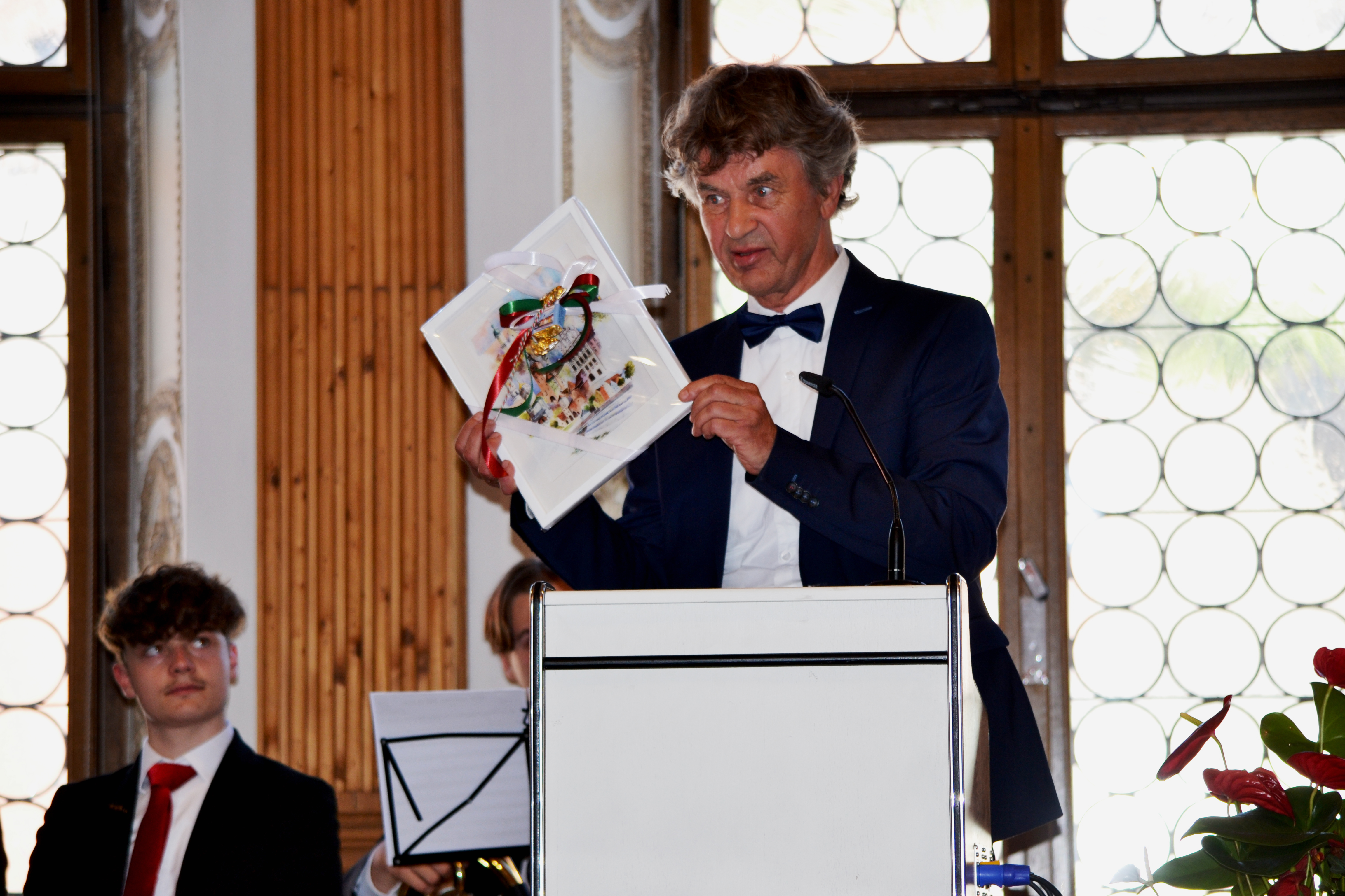 Herr Kirchner Herr Kirchner steht auf der Bühne bei seiner Ansprache und präsentiert sein erhaltenes Abschiedsgeschenk