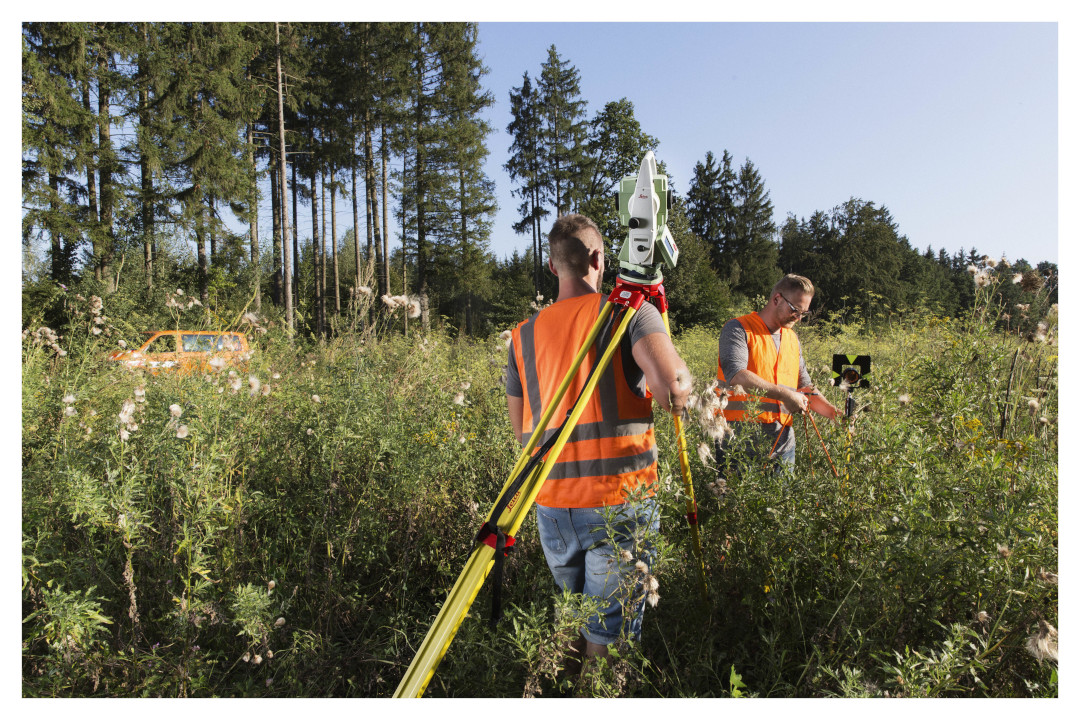 Außendienstmitarbeiter bei der Arbeit Zwei Außendienstmitarbeiter stellen in einer hochbewachsenen Waldschneise  Vermessungsgeräte auf