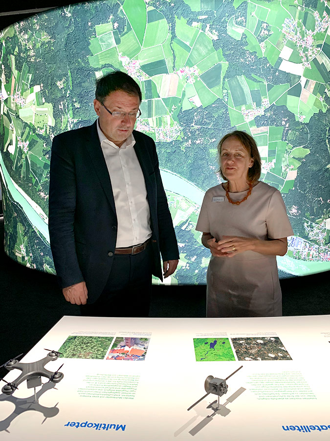 Eröffnung der Sonderausstellung im Bayerischen Landesluftbildzentrum Zwei Personen stehen hinter einer Ausstellungstheke mit Text und 3D-Objekten