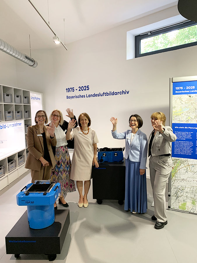 Eröffnung der Sonderausstellung im Bayerischen Landesluftbildzentrum Fünf Frauen stehen im Ausstellungsraum und winken in die Kamera